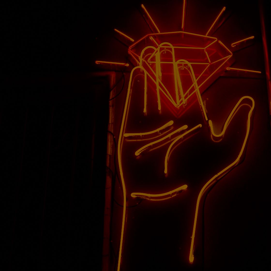A orange neon sign of a hand with fingers reaching for a diamond